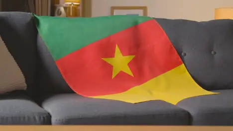 Flag Of Cameroon Draped Over Sofa At Home With Football Ready For Match On TV 4