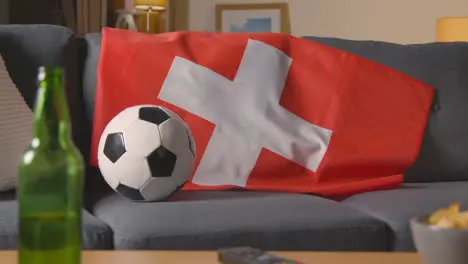 Flag Of Switzerland Draped Over Sofa At Home With Football Ready For Match On TV