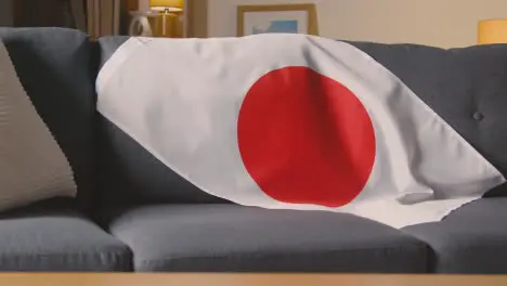 Close Up Of Flag Of Japan Draped Over Sofa At Home Ready For Match On TV 1