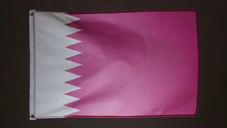 Studio Shot Of Flag Of Qatar Collapsing Against Black Background