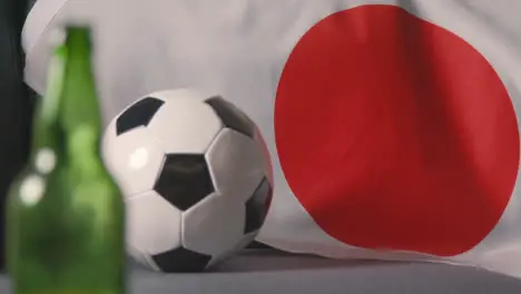 Close Up Of Flag Of Japan Draped Over Sofa At Home With Football Ready For Match On TV