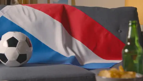 Flag Of Holland Draped Over Sofa At Home With Football Ready For Match On TV 1