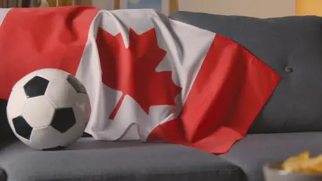 Flag Of Canada Draped Over Sofa At Home With Football Ready For Match On TV 1