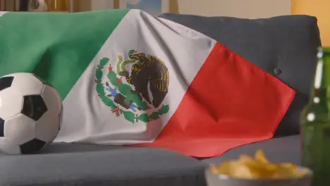 Flag Of Mexico Draped Over Sofa At Home With Football Ready For Match On TV 1