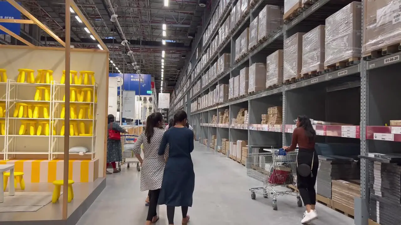 A girl carrying a shopping cart and walking down the aisle with her friends who are walking beside her and crossing multiple section of the stores