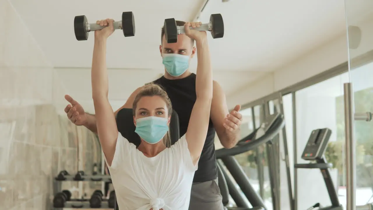 Young Athlete Woman Lifts Weights And Man With Face Mask Exercising In The Gym