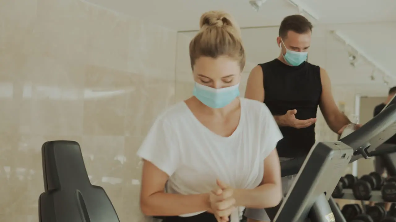 Young Athlete Female And Male With Face Mask Using Hand Sanitizer And Exercise Machines In The Gym