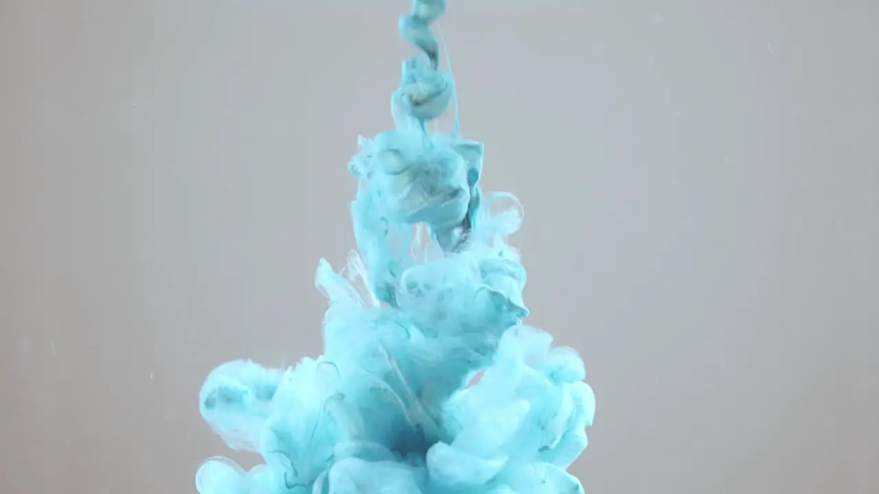 Blue paint squirted into clear liquid on grey background slow motion