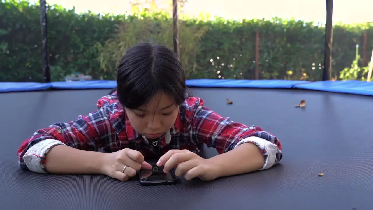 girl lying down on trampoline using her phone still low angle shot