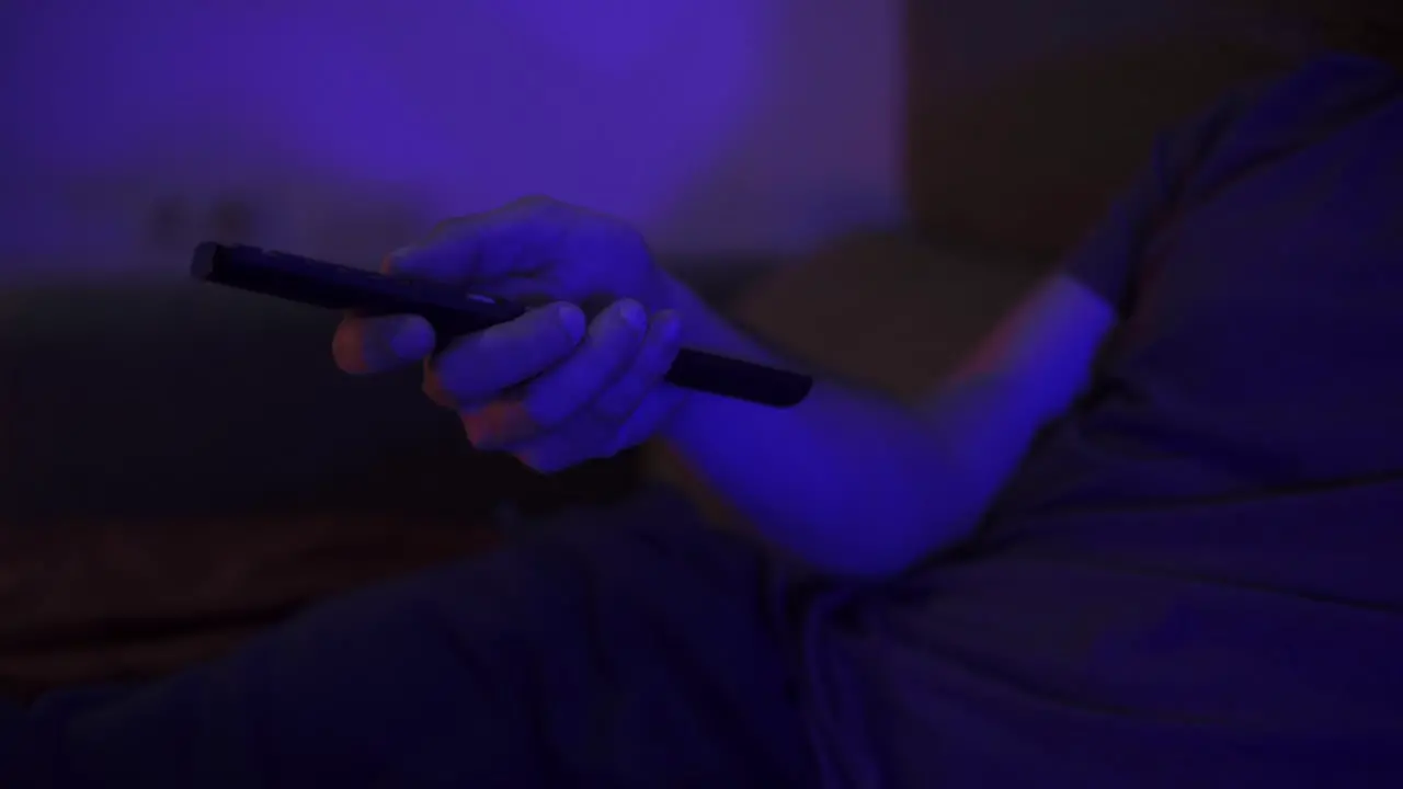 Close-up shot of a man pressing buttons on a tv remote with the room flickering with light