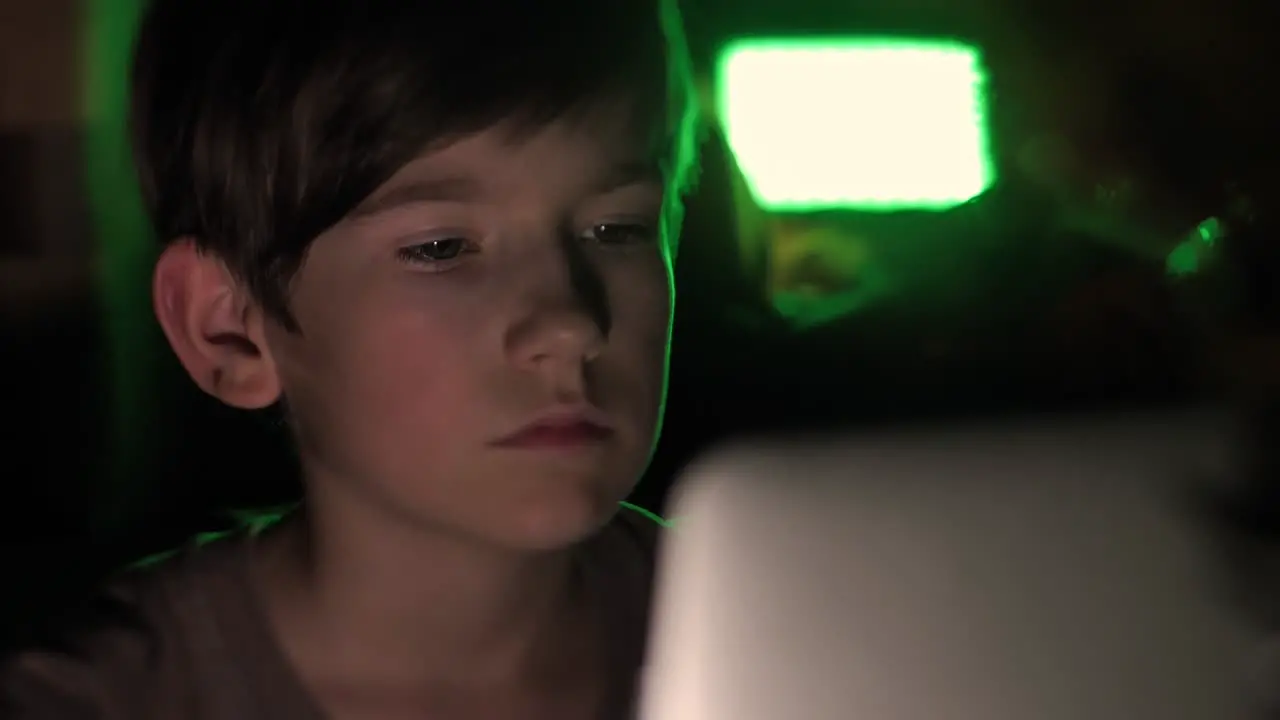 A child sits in the dark at a computer