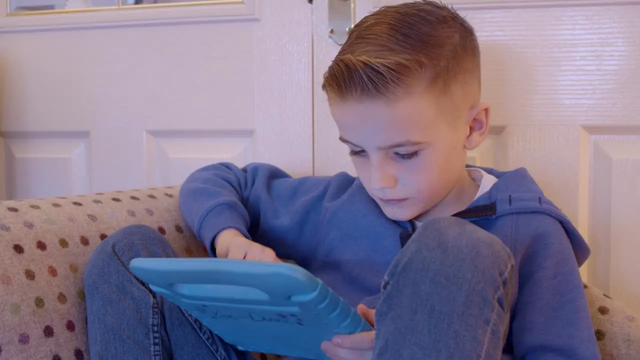 Close up of a child playing games on a tablet while sitting on a sofa at home