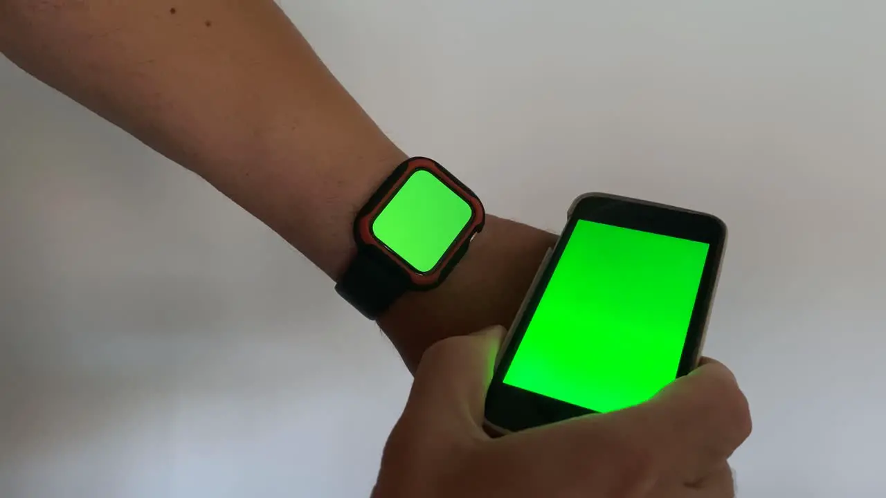 Fit man scrolling pages on green phone and checking green watch while taking a break in work