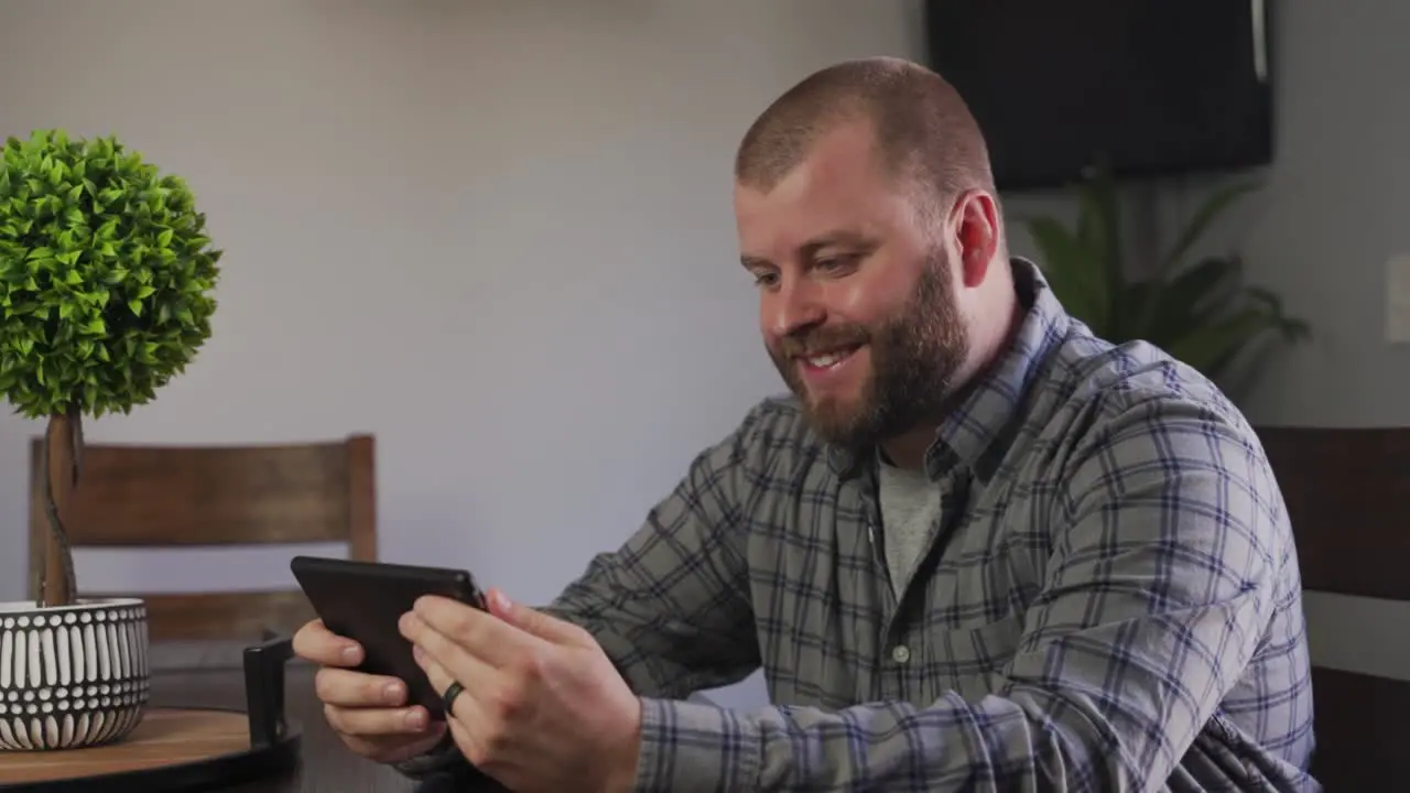 A Friendly Looking Bearded Young Adult Waving Hand While Video Chatting With Someone On His Tablet At Home