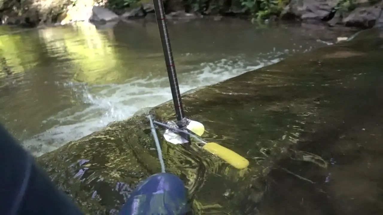 A scientist with boots tries to measure the flow of a river with a magnetic probe and a meter