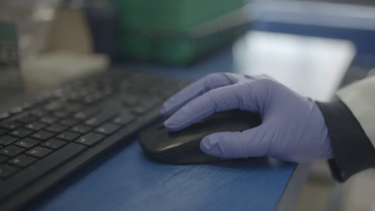 Scientist in lab using mouse for computer research with gloves on hand