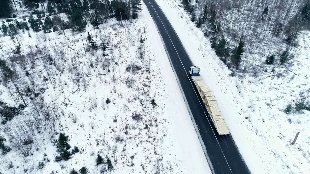 Aerial drone shot of long lorry driving on a road in the middle of forest in winter