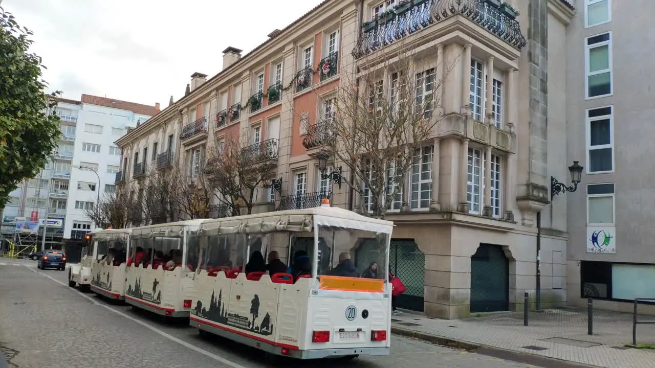 tourists on the tram passing through the historic pilgrimage city nice buildings on the street with trees and people strolling shot blocked Santiago de Compostela Galicia