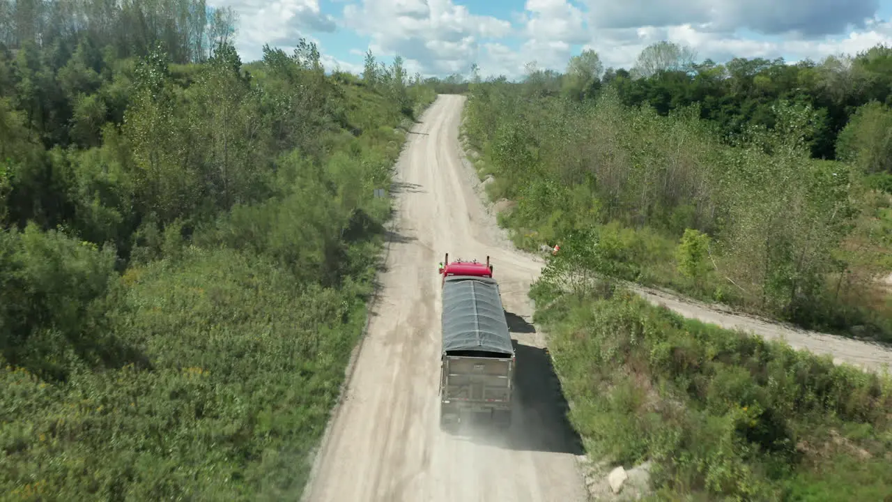 A haulage vehicle drives along a dusty rural road on a sunny day