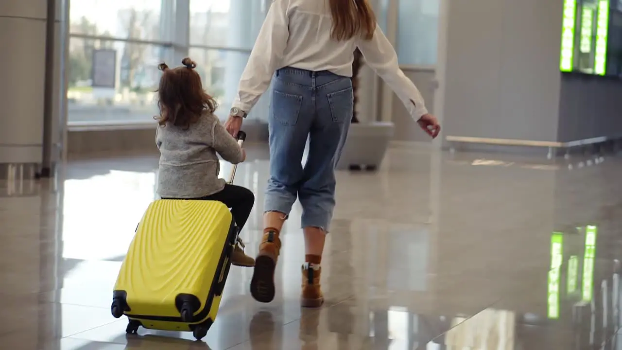 Airport Terminal Young Unrecognizable Mother Riding Her Cute Daughter On A Small Yellow Suitcase