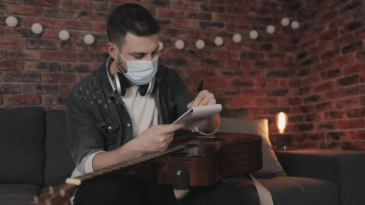 Young Musician Man With Medical Face Mask Creating Music Having Ideas Taking Notes At Home During Lockdown Due To The Covid 19 Pandemic