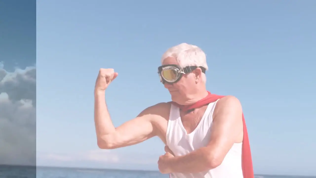 Animation of clouds over happy senior caucasian man wearing superhero costume on beach