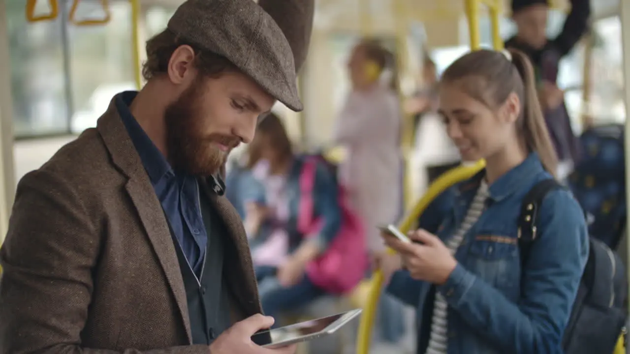 Young Man With Beret Using Smartphone Standing In The Bus In The Background A Young Girl Standing Chatting With Smartphone