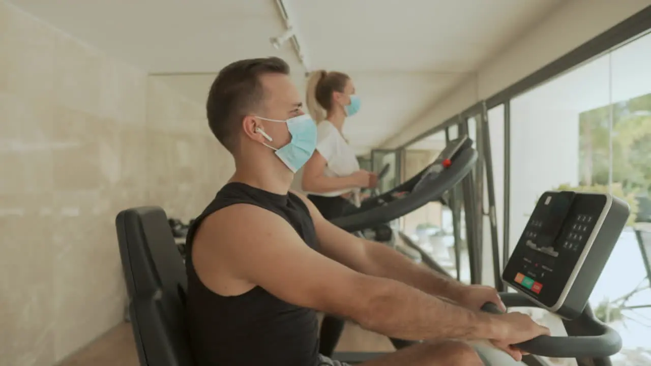 Athlete Male And Female With Face Mask Using Exercise Machines In The Gym