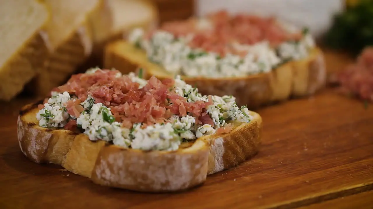 Tasty homemade bruschetta with ham on white cheese served in a wooden cutting board macro close up slider movement