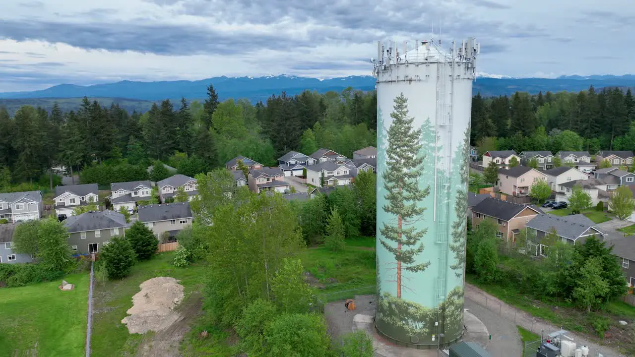 Drone shot of a suburban water tower with a large tree mural on the side of it