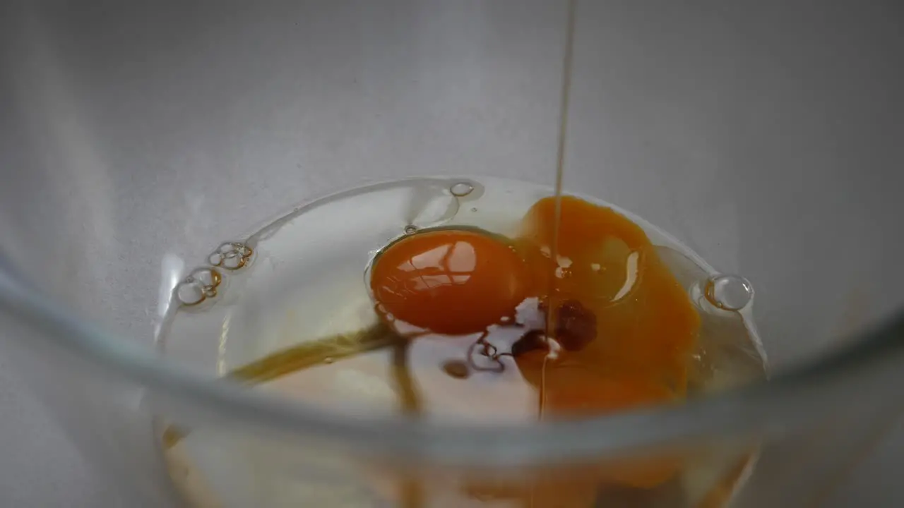 Person pouring vanilla essence onto metallic spoon and sprinkling over flour and baking mix