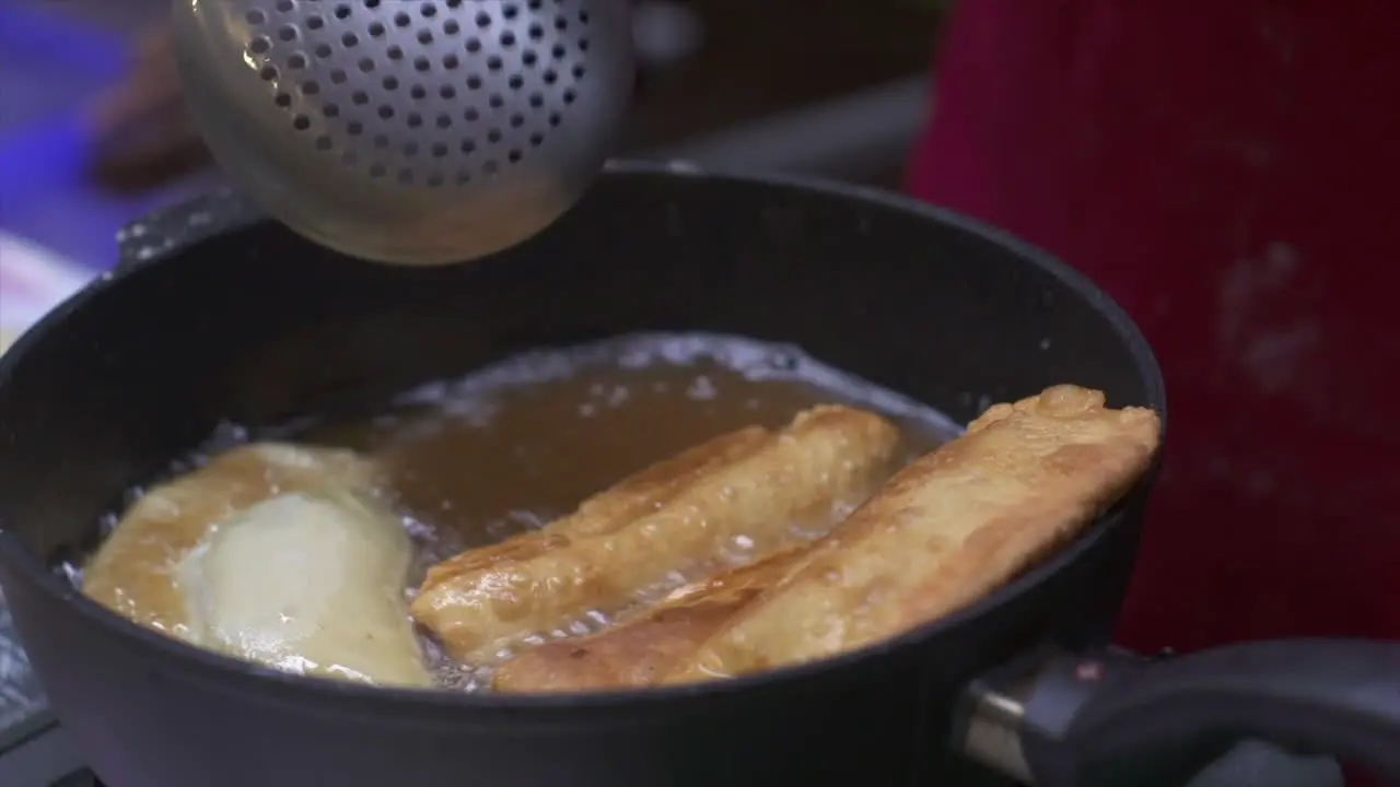 Meat roll and samosa deep fried and stirred in oil hot oil filmed as close up in handheld style