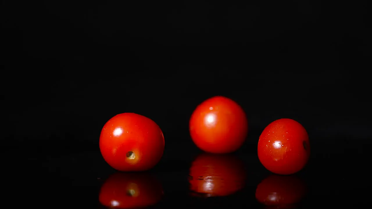 Side view of three tomatoes falling in slowmotion on a black reflective surface