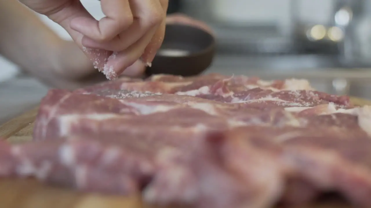 Close shot of fingers putting salt on raw meat in the kitchen