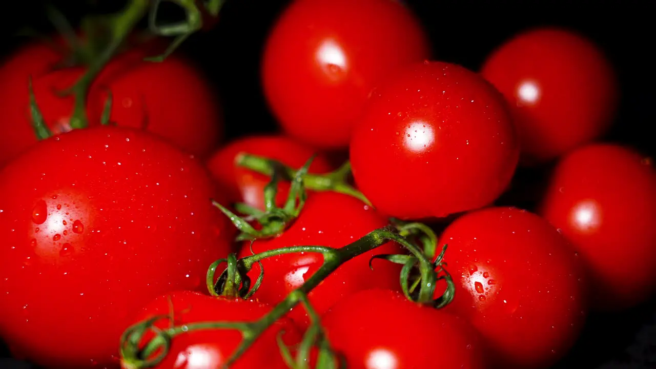 close up of a male hand picking up a tomato from a stack of tomatoes with a black background