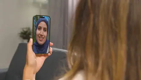 Close Up Of Woman Sitting On Sofa At Home Having Video Call With Female Muslim Friend On Mobile Phone