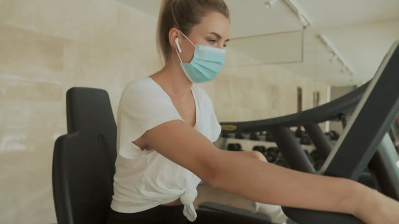 Athlete Female With Face Mask Working Out With An Exercise Machine And Drinking Water In The Gym