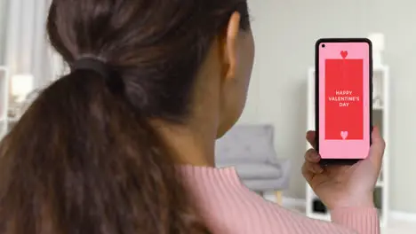 Close Up Of Woman At Home Looking At Happy Valentine's Day Message On Mobile Phone