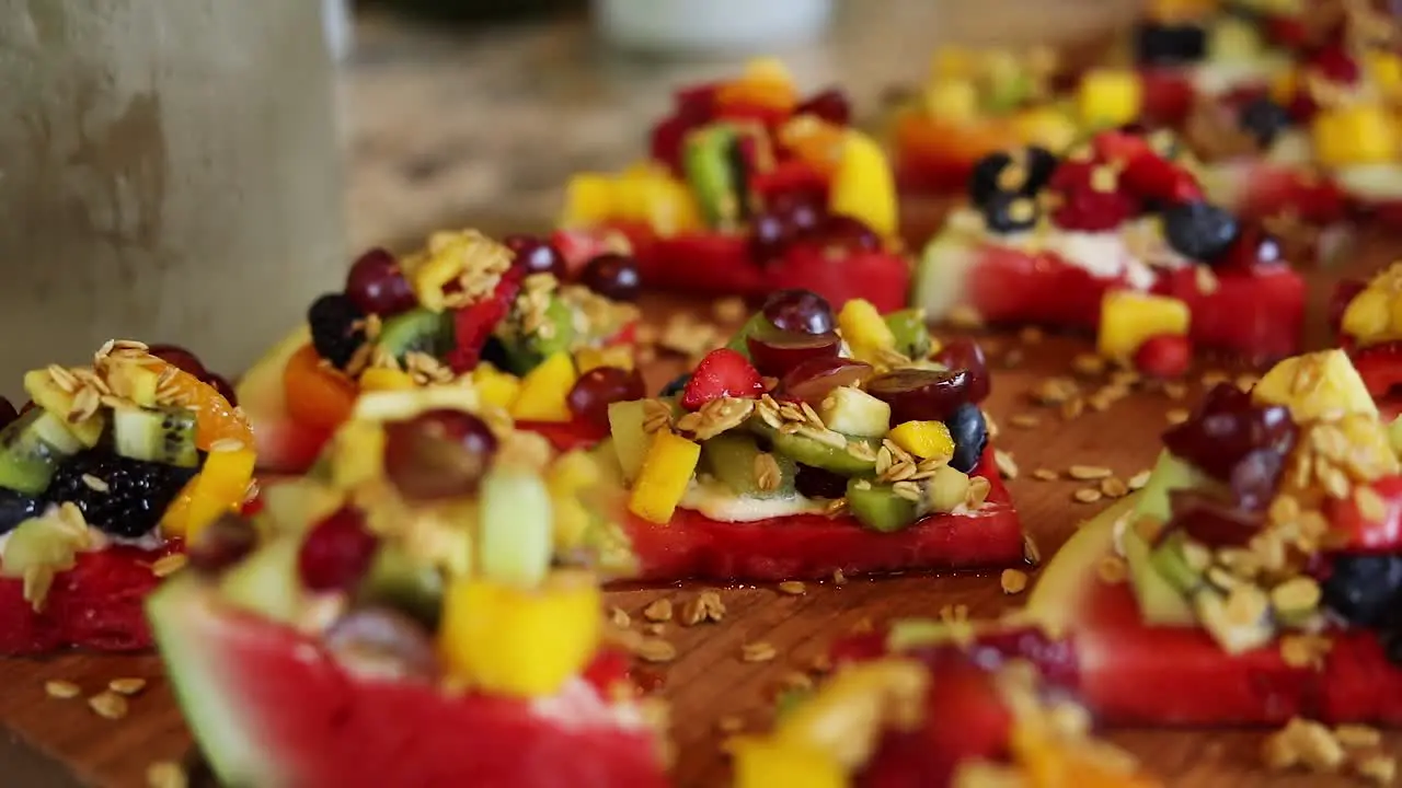 Panning Shot over slices of watermelon with a yogurt cream on top along with granola and a variety of fruits including blueberries pineapple strawberries and raspberries