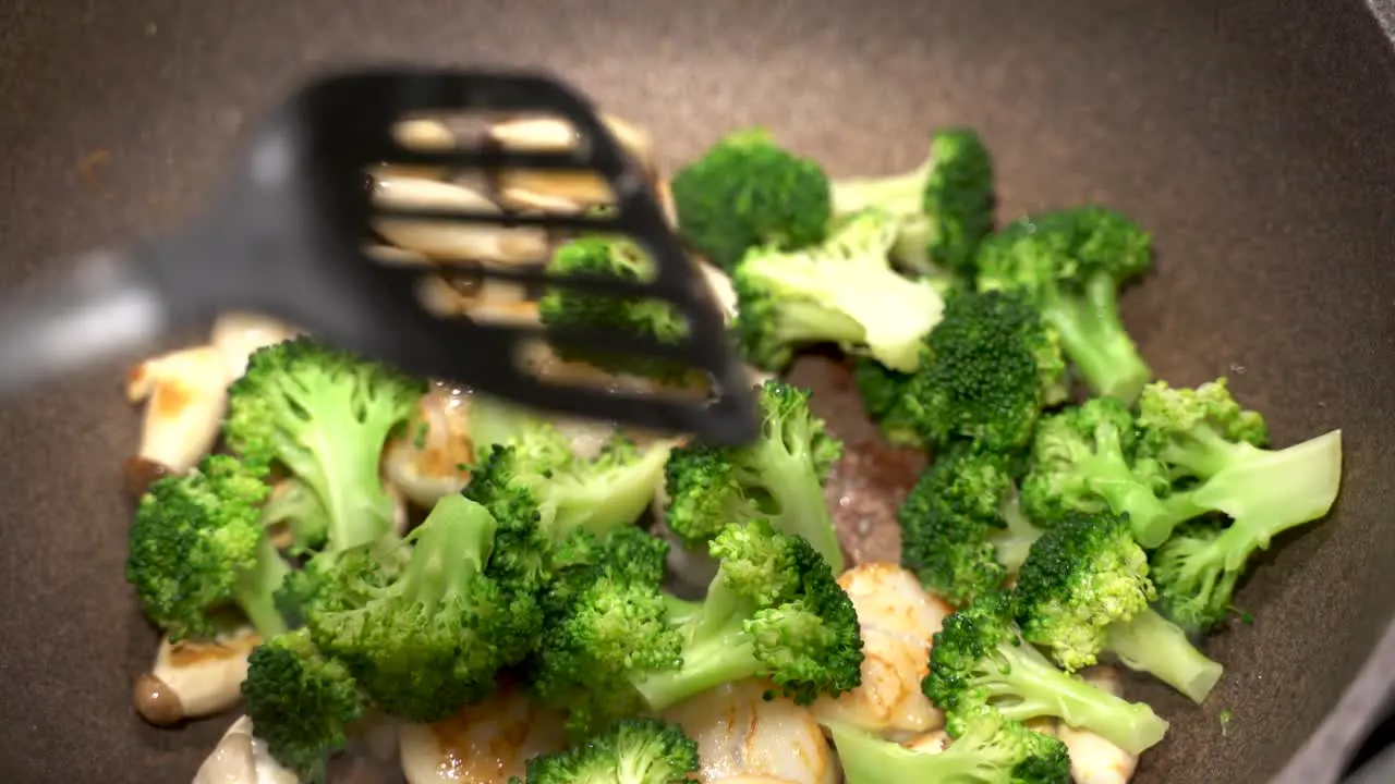 Delicious scallops broccoli and mushrooms being fried cooked in a large pan