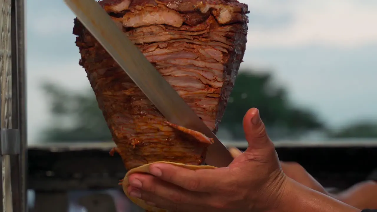 Taquero cutting carne al pastor meat pork raw fresh authentic from trompo kebab shawarma grilled asada tortilla in hand hot recipe latin mexico