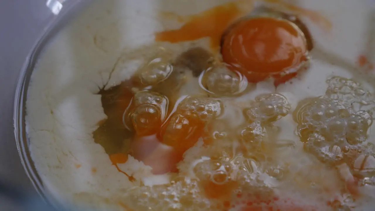 Slow motion pan around baking ingredients of egg milk and oil in glass bowl with low depth of field