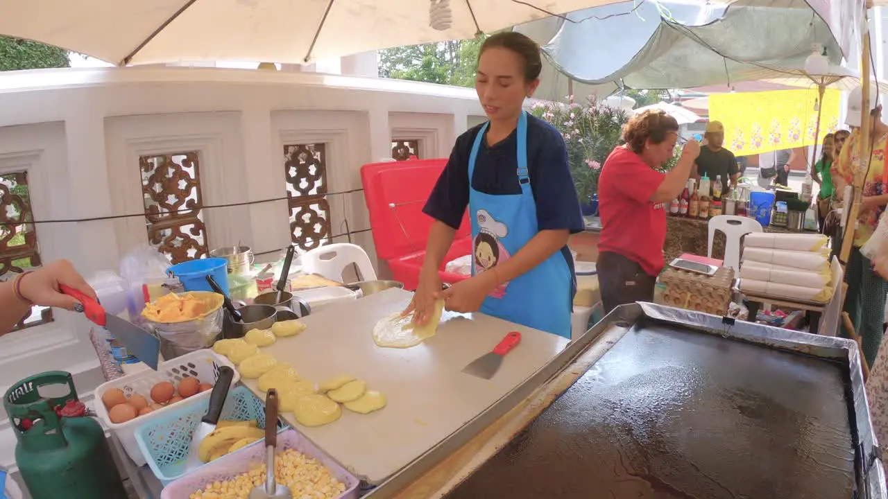 Thai street food women preparing and bakes pancakes sweet roti with bananas eggs and butter