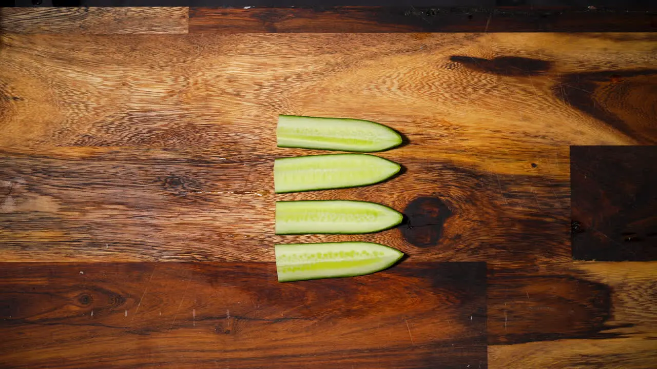 Top view of a male hand slicing two pieces of cucumber perpendicular in the middle