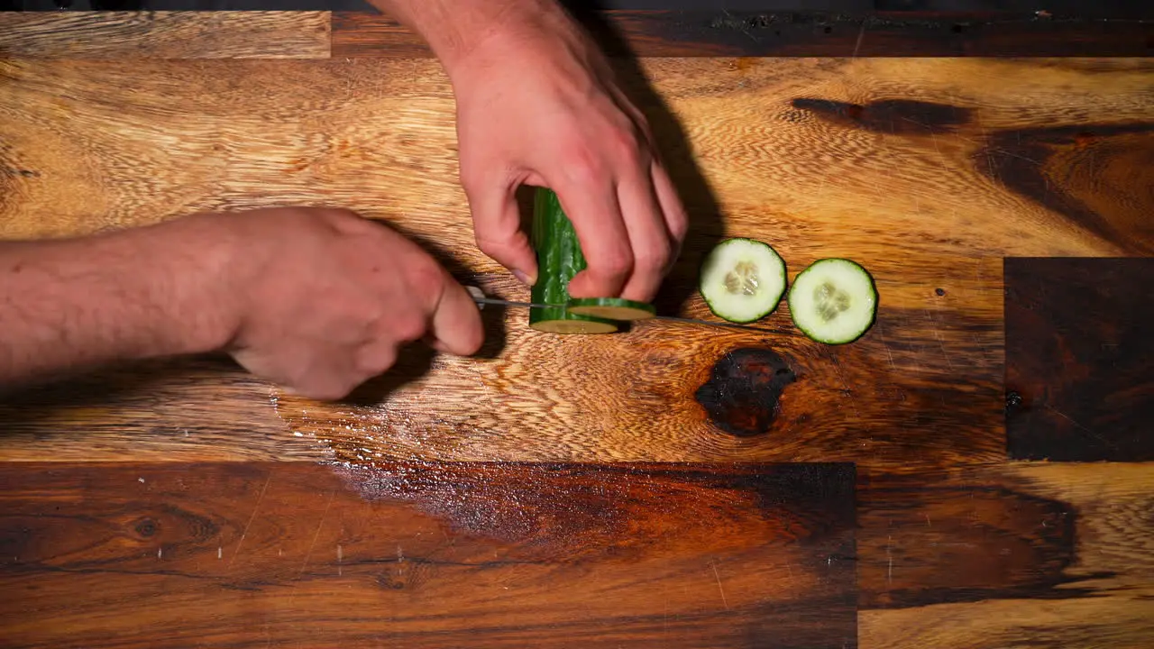 Top view of a male hand chopping a fresh cucumber on cutting board in slowmotion