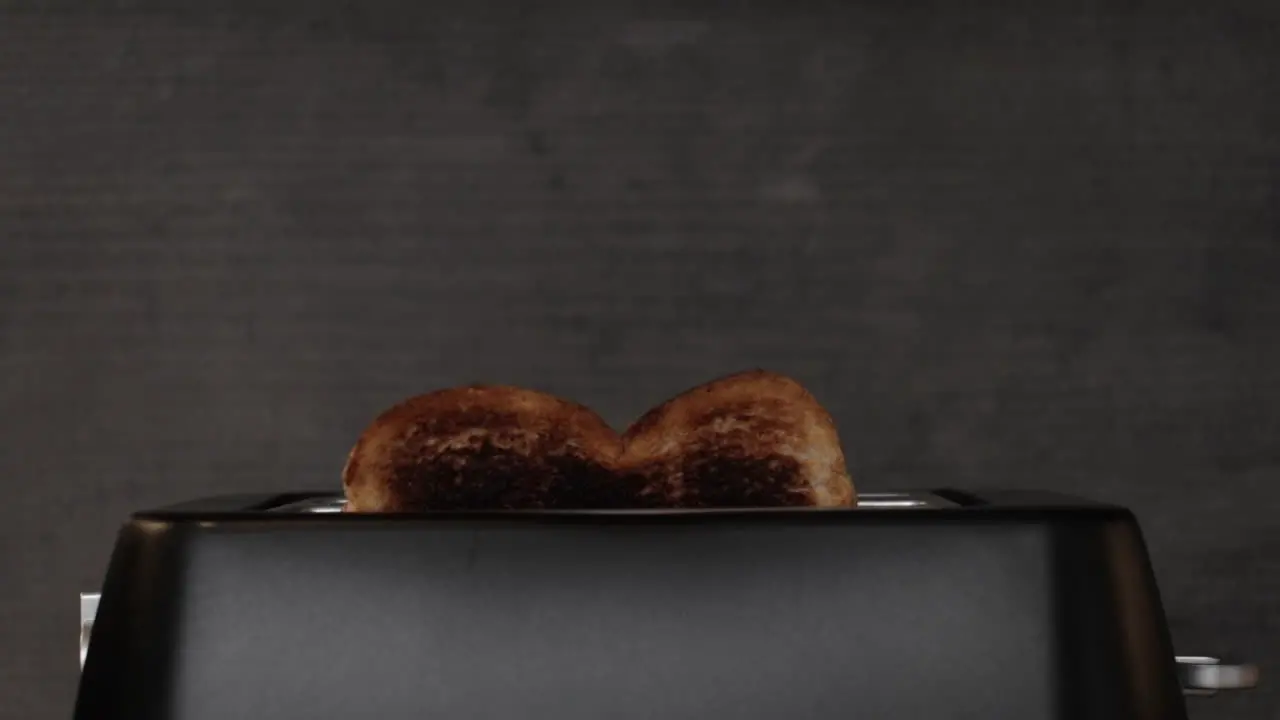 A slow-motion shot of some burnt toast popping out of a black matte toaster with smoke rising from it