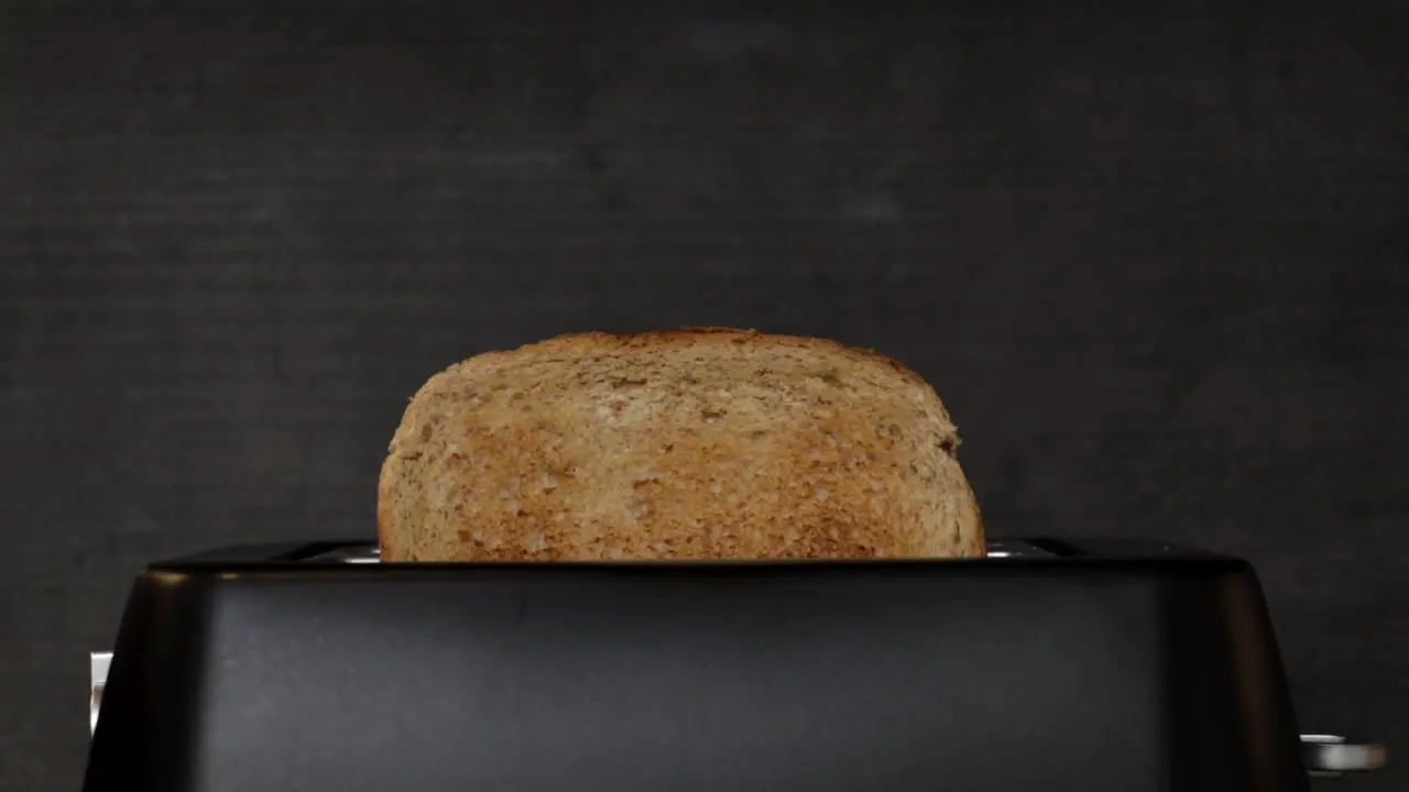 A slow-motion shot of some lightly browned toast popping out of a black matte toaster