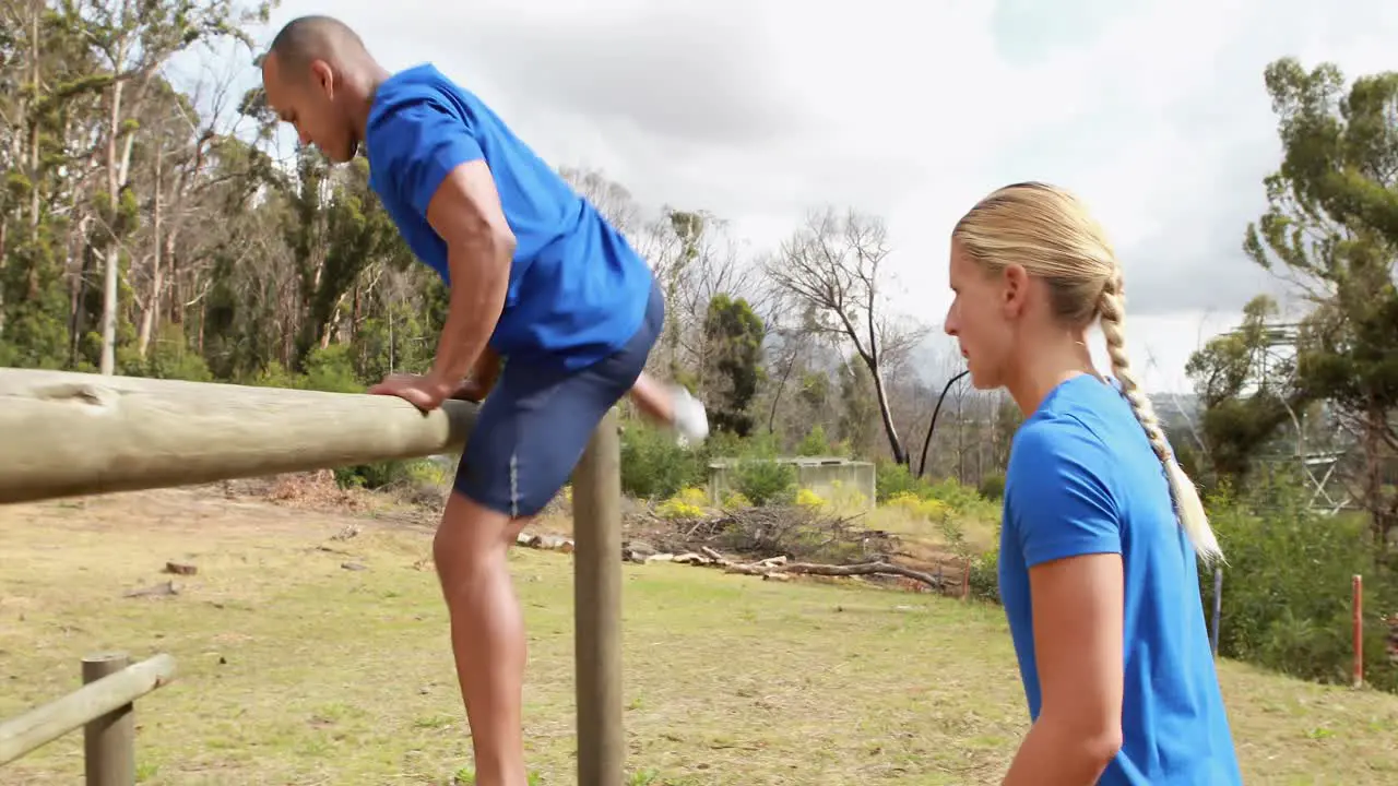 Male trainer assisting woman to climb a hurdles during obstacle course