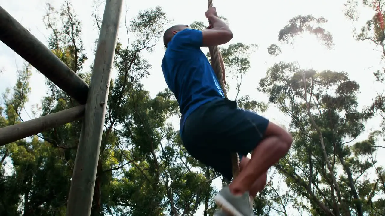 Fit man climbing rope during obstacle course