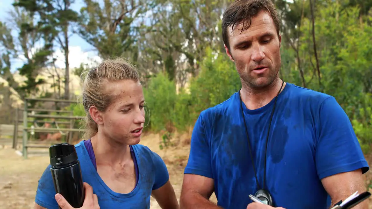 Male trainer assisting woman on clipboard during obstacle course